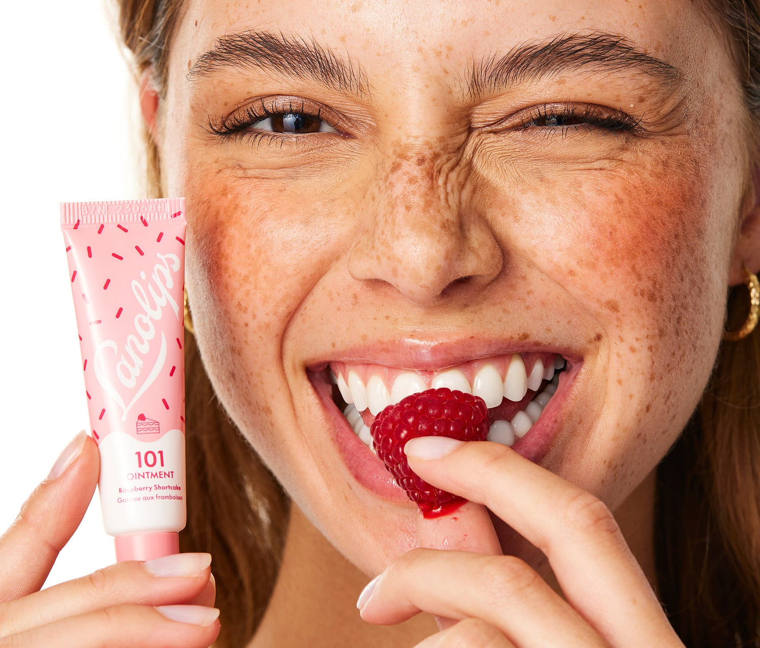 A model biting into a rapsberry while holding a tube of Lanolips 101 Ointment Multi Balm in Raspberry Shortcake, which is part of the Lanolips 101 Delicious flavours range. Made with lanolin, vitamin e and all natural raspberry flavour, it leaves your lips feeling perfectly hydrated.
