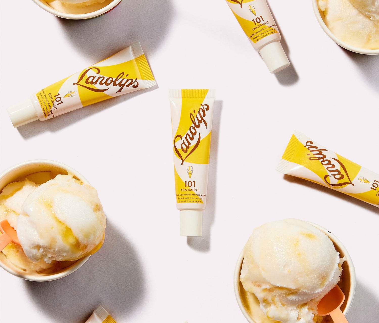 Lanolips x MESSINA 101 Ointment Multi Balm in Salted Coconut & Mango Sorbet, surrounded by scoops of creamy mango and coconut sorbet in small cups. The balm's yellow and white packaging complements the dessert-inspired theme. Made with lanolin, vitamin e and natural coconut oil and mango fruit extract, for a naturally sweet hydration boost throughout the day. The super rich balm gives long lasting hydration for dry and chapped lips, skin patches, cuticles, elbows and more.
