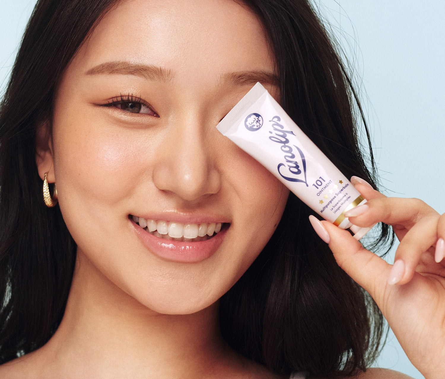 A model holds a tube of Lanolips The Original 101 Ointment Multipurpose Superbalm over one eye. This 100% natural, multi-award-winning balm is a powerful multi-tasker with 101 uses - from ultra-hydrating lips to soothing dry skin. Voted ‘The World’s Best Lip Balm,’ it’s a hard-working formula enriched with pure lanolin, which mimics the skin’s natural oils to deeply nourish and lock in moisture. Perfect for soft, smooth, and healthy lips.