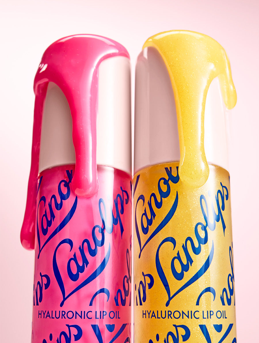 Two Lanolips Hyaluronic Lip Oils in Honey and Raspberry shades, with lip oil dripping from the tops, against a soft pink gradient background