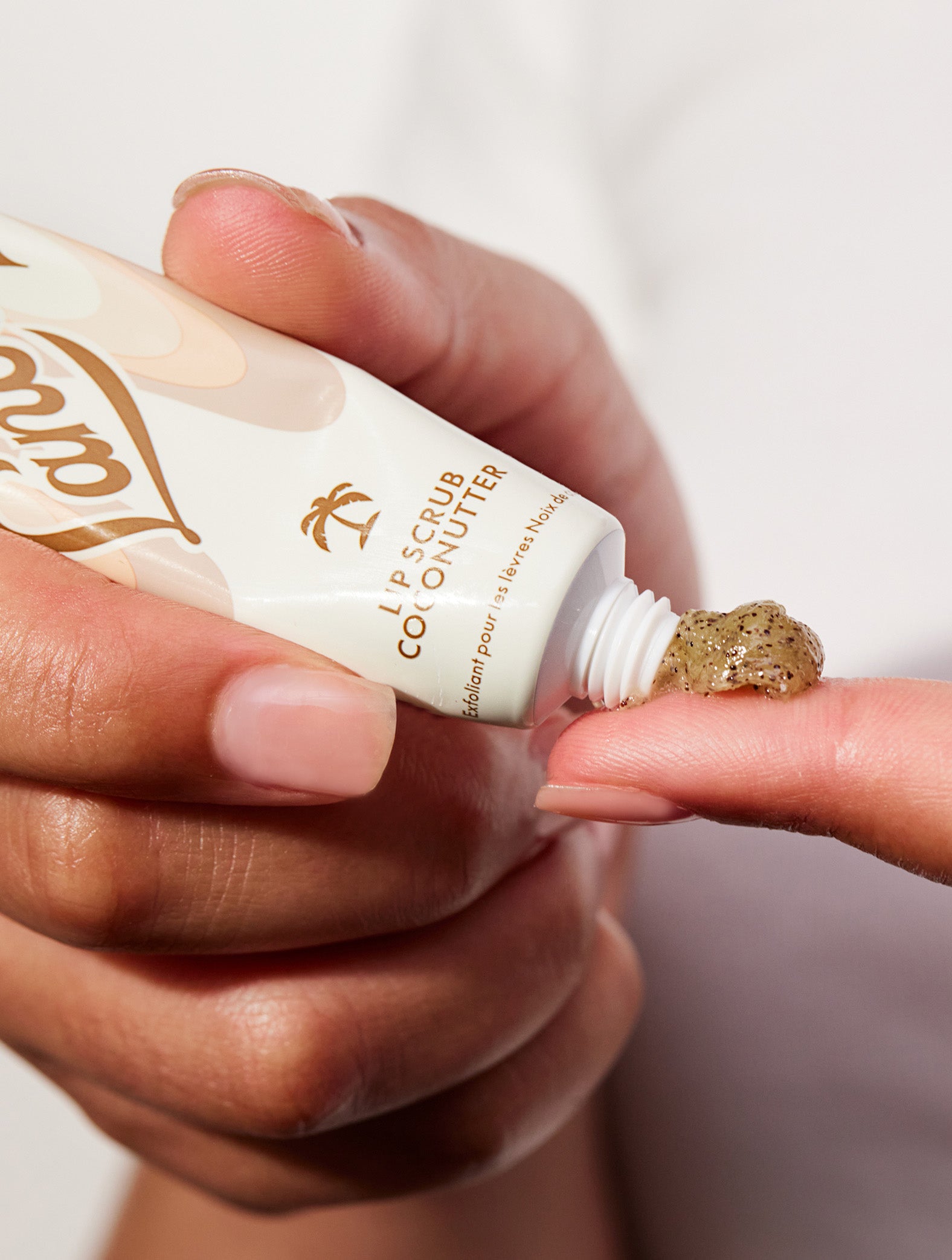 Model holding lanolips lip scrub in coconutter in her hand showing the texture of the product.