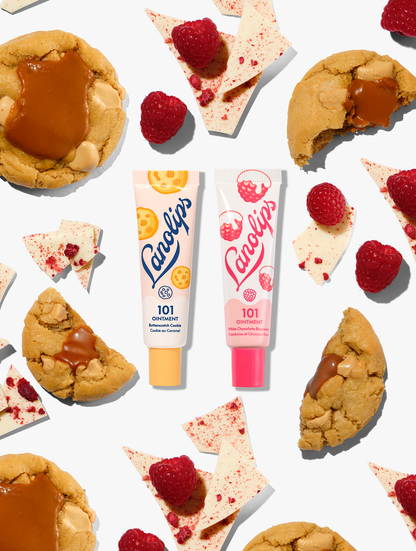 Lanolips 101 Delicious collection duo featuring 101 Ointment Multi-Balms in Butterscotch Cookie and White Chocolate Raspberry. The two natural lanolin balm tubes are pictured together amongst chewy caramel biscuits, fresh raspberries, and shards of white chocolate.